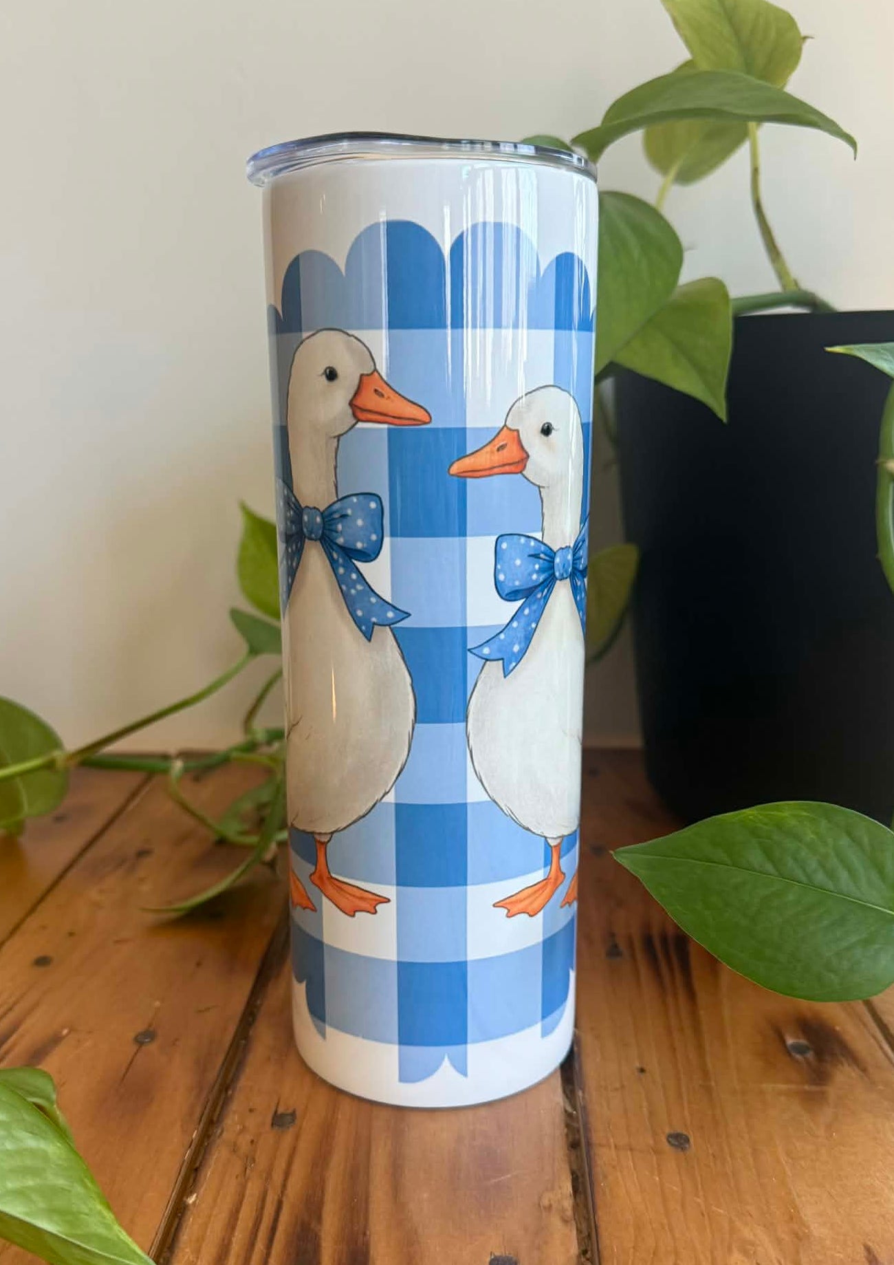 Tumbler with duck design on a wooden surface with plants in the background