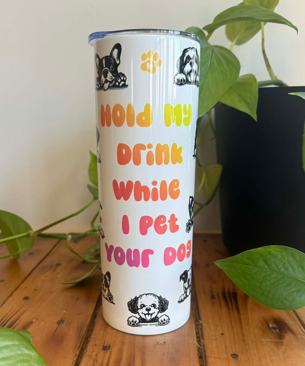Tumbler with humorous text and dog illustrations on a wooden surface with plants.