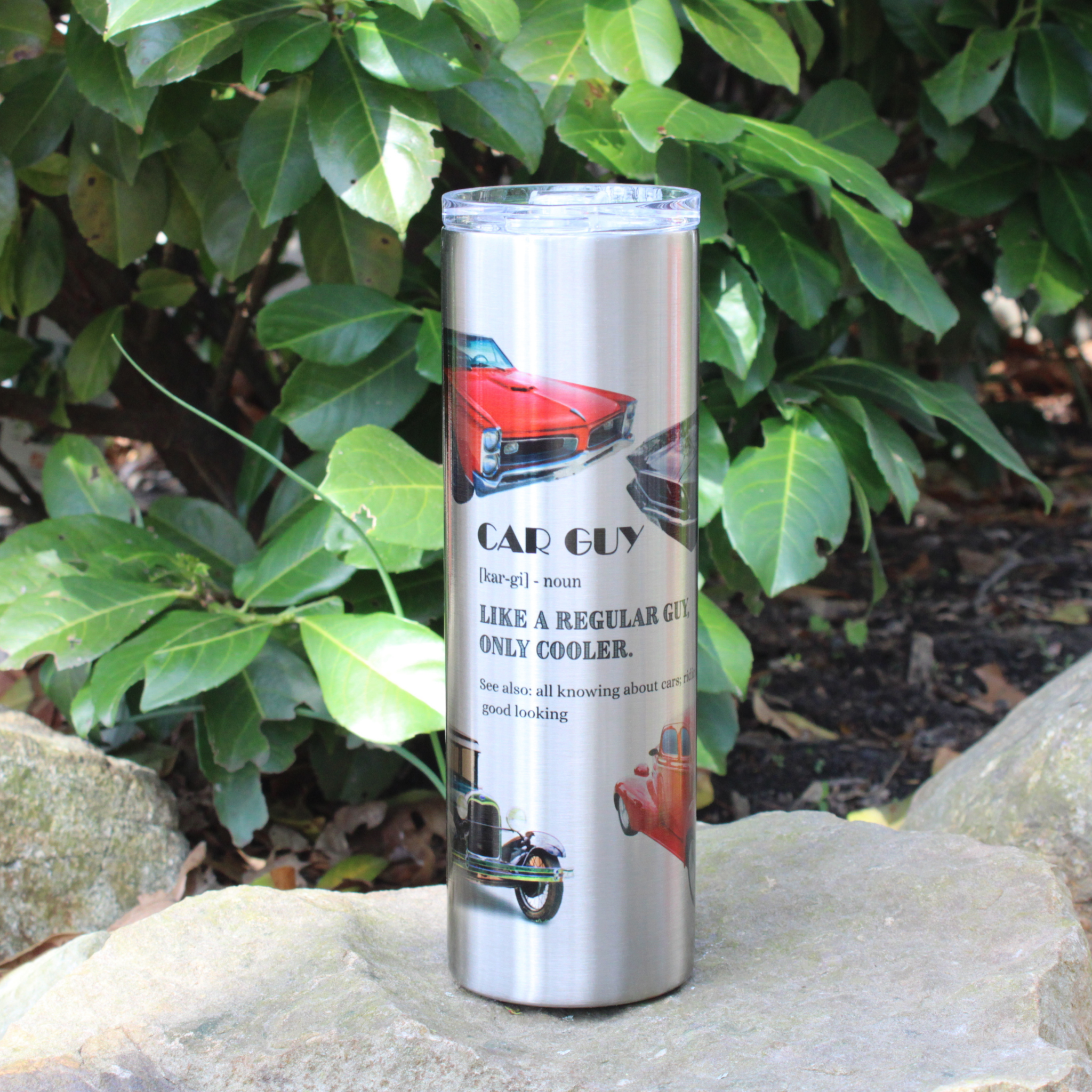 Metal tumbler with 'Car Guy' design on a stone surface with green foliage in the background