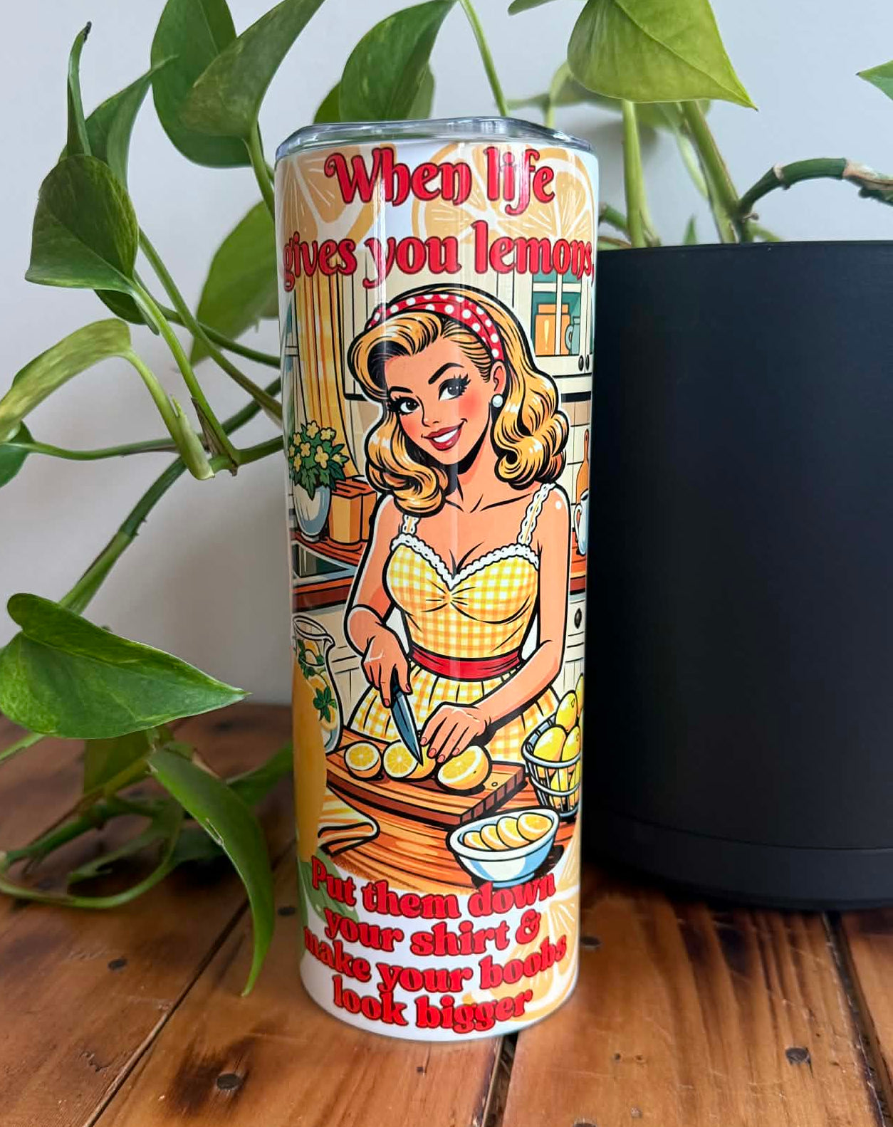 Tumbler with vintage-style kitchen design featuring a woman with lemons and humorous text, placed on a wooden surface with a plant in the background.