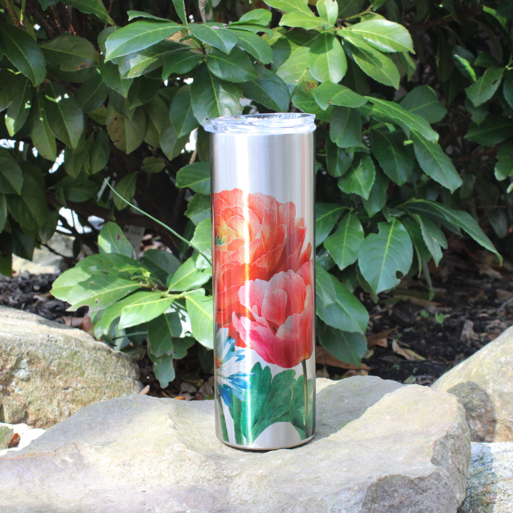 Tumbler with floral design on a rock with green foliage in the background