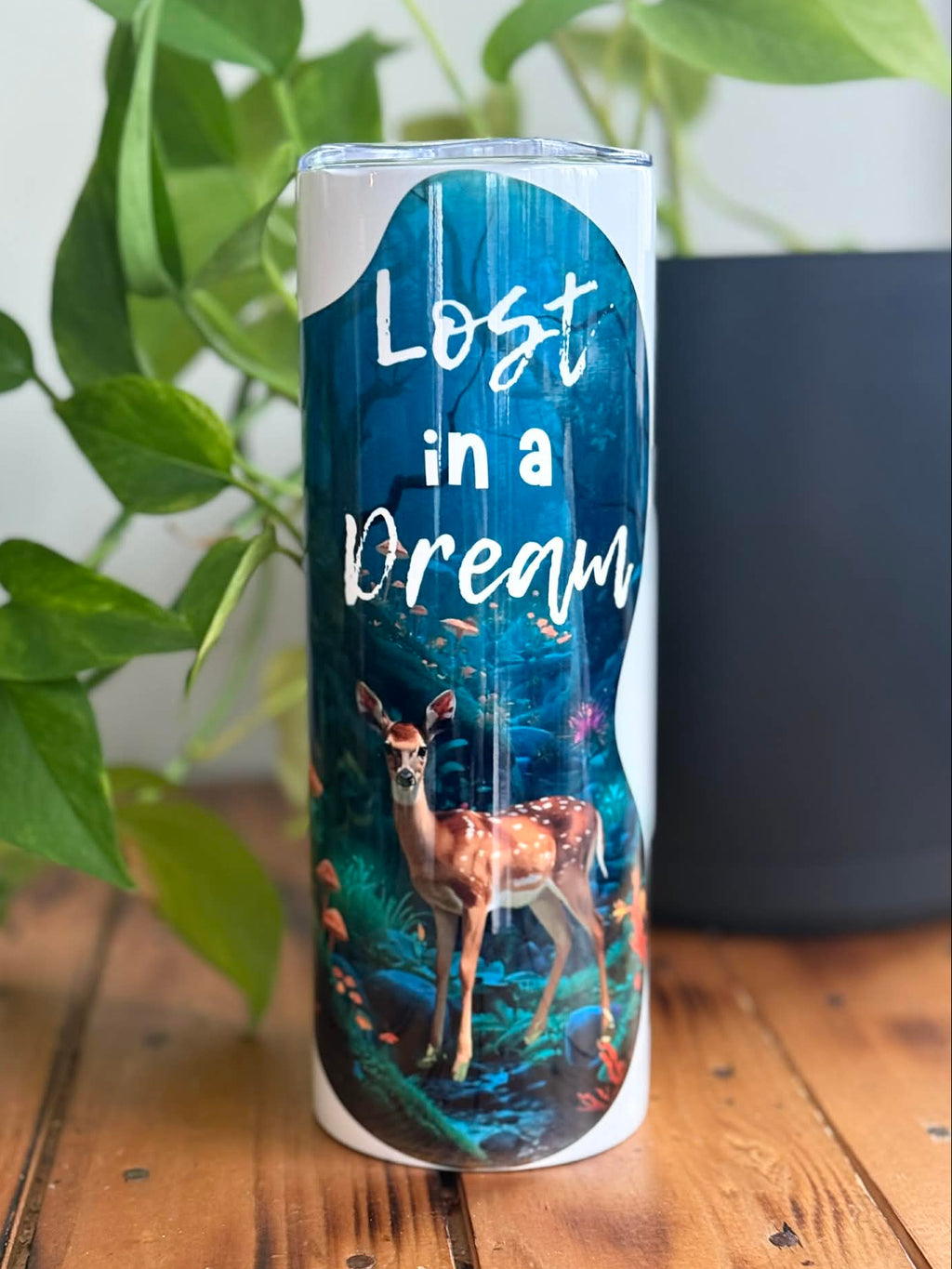 Tumbler with 'Lost in a Dream' text and deer design on a wooden surface with plants in the background