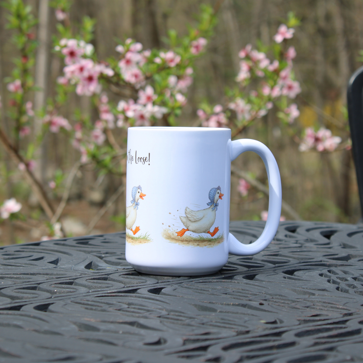 White mug with goose in bonnet design on a black metal table with blurred floral background