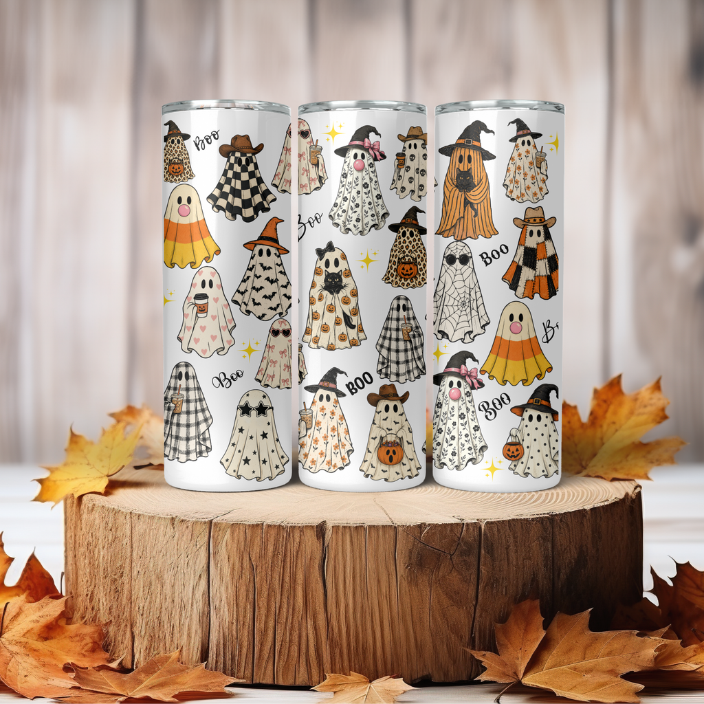 Three white insulated tumblers with a Halloween ghost pattern, displayed on a rustic wooden log slice with autumn leaves.