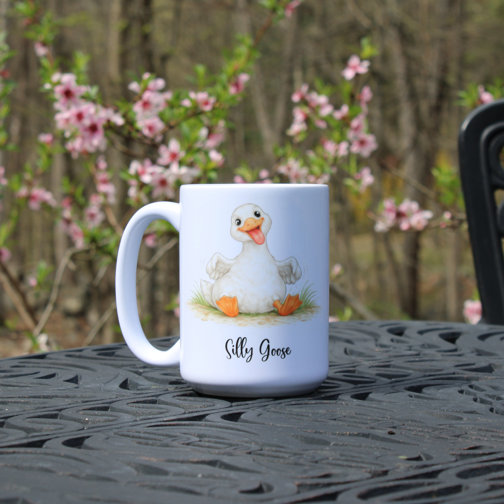 White mug with a goose illustration and 'Silly Goose' text on a black metal table with a blurred floral background.