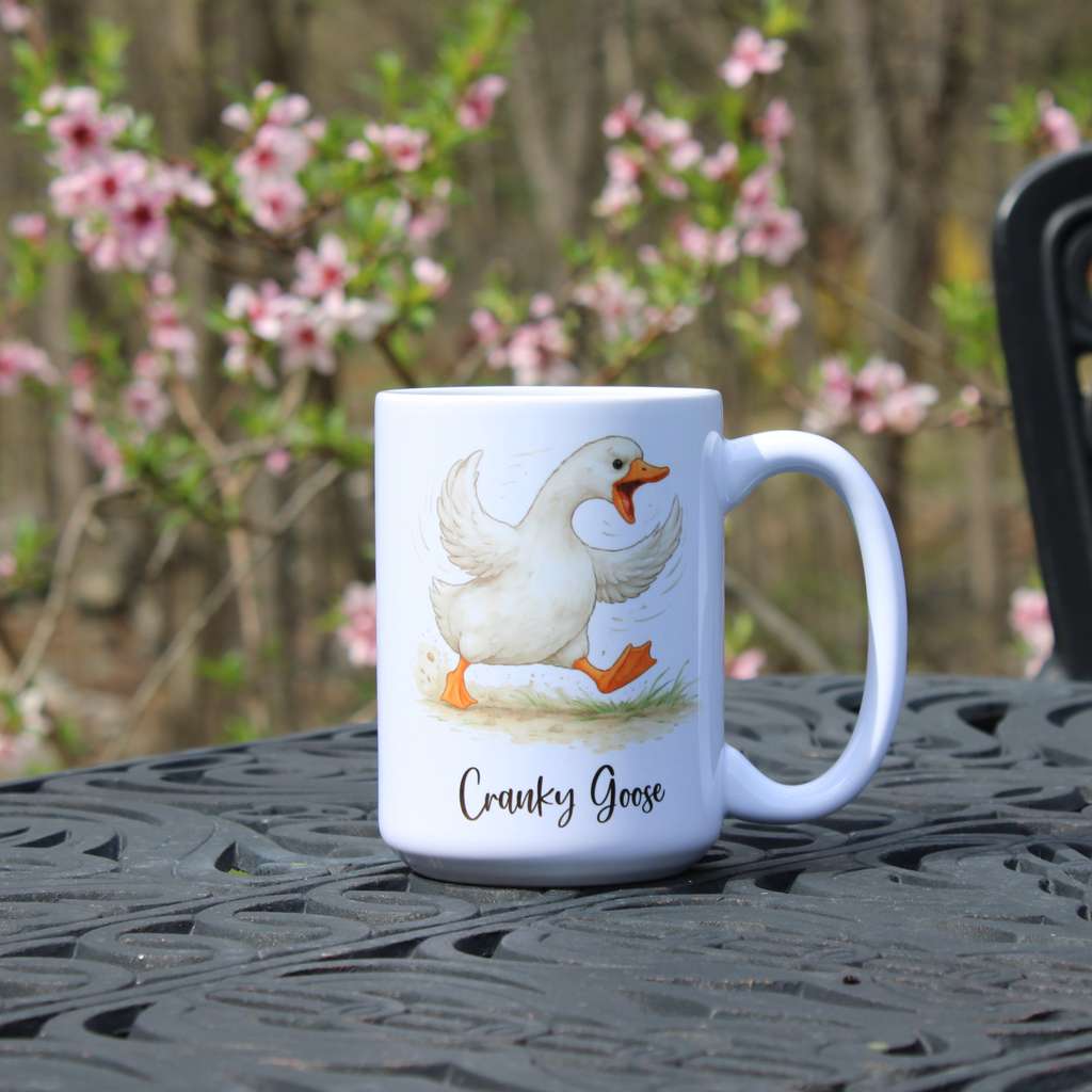 White mug with a  goose design and 'Cranky Goose' text on a table outdoors.