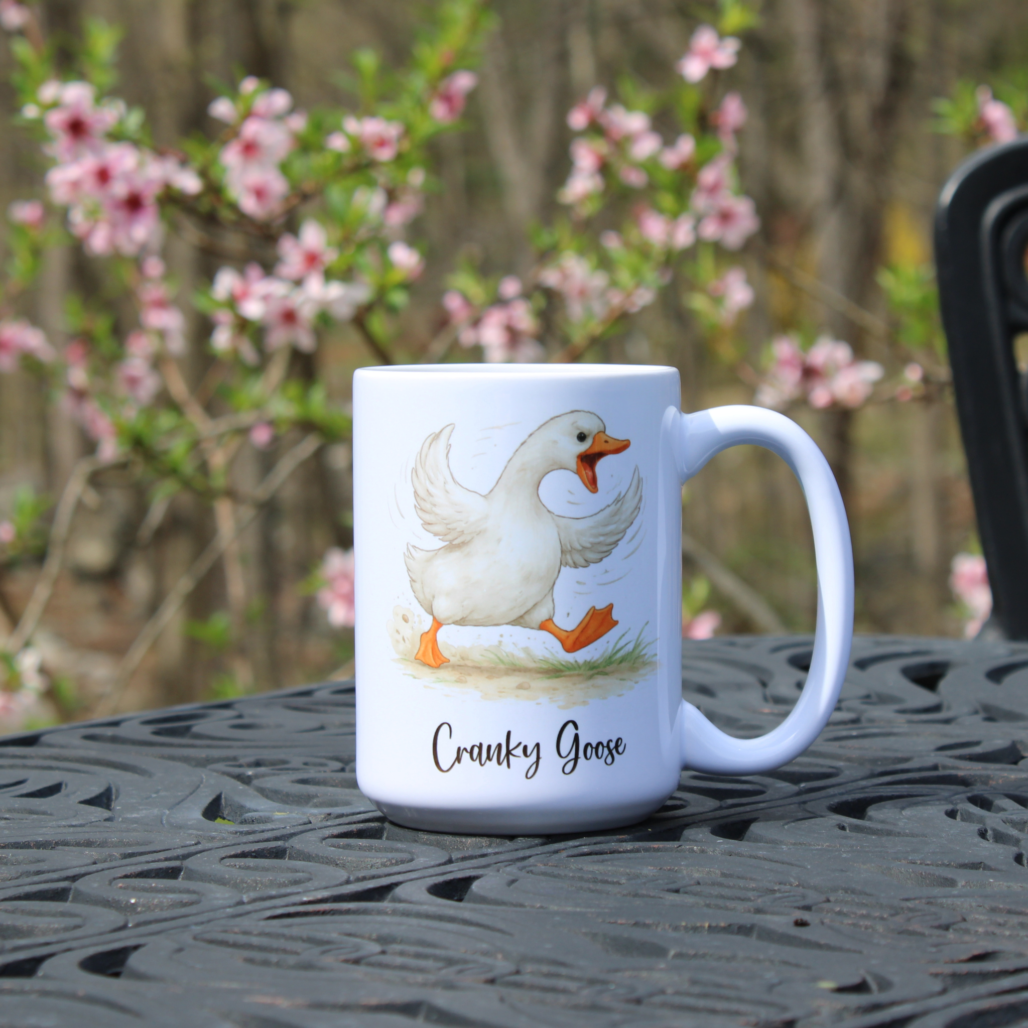 White mug with a  goose design and 'Cranky Goose' text on a table outdoors.
