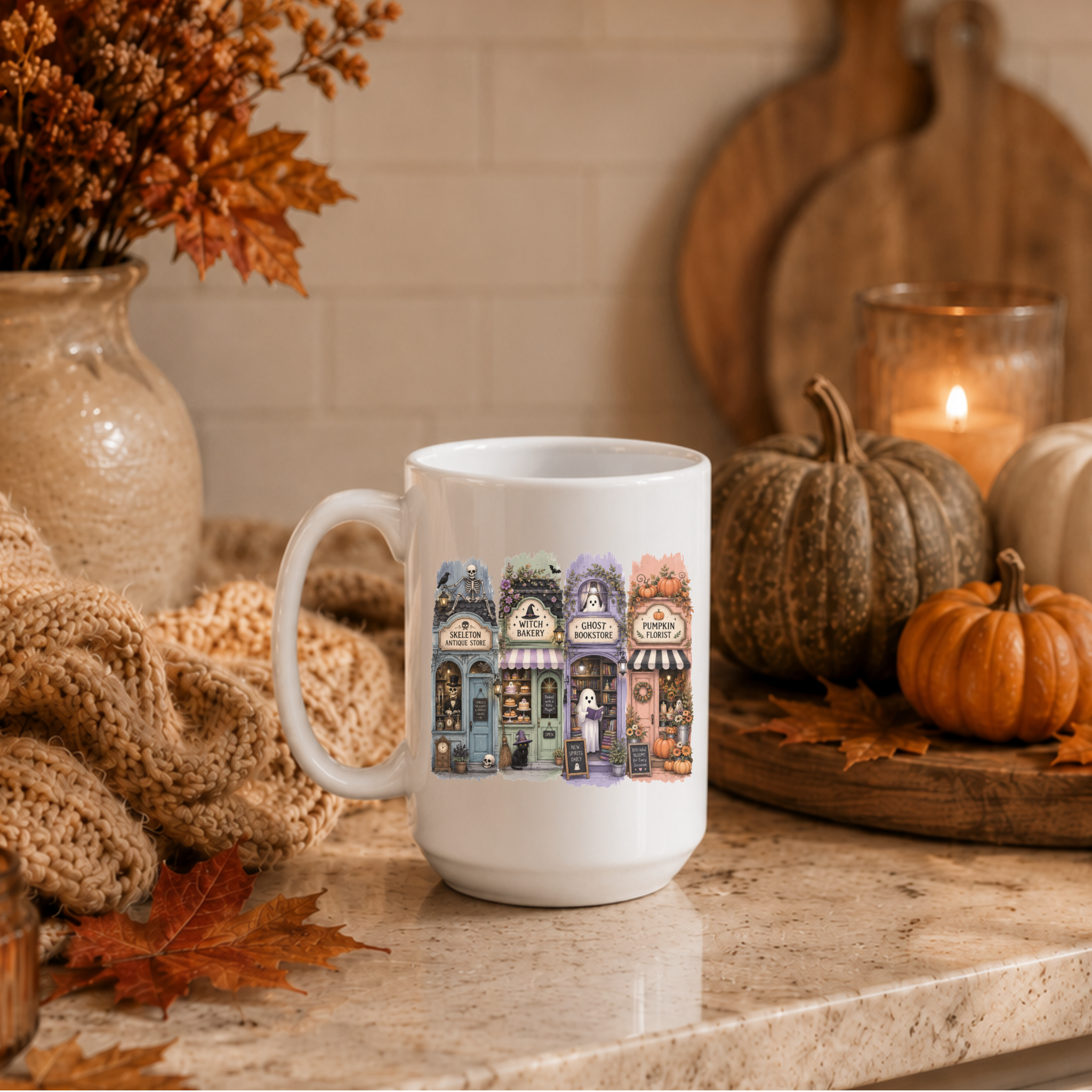 A white ceramic mug with a colorful illustration of four spooky storefronts, styled on a kitchen counter with autumn decorations including pumpkins, a knitted blanket, and a candle.